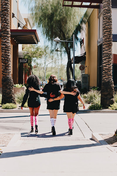 Three stylists posing by a tree wearing pink and white salon-themed compression socks