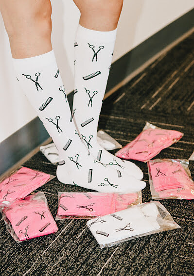 Stylist wearing white Salongevity compression socks surrounded by hand-packed pink and white pairs